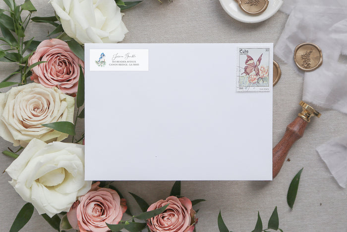 White envelope with a stamp and personalized address on a table with flowers and stationery items.