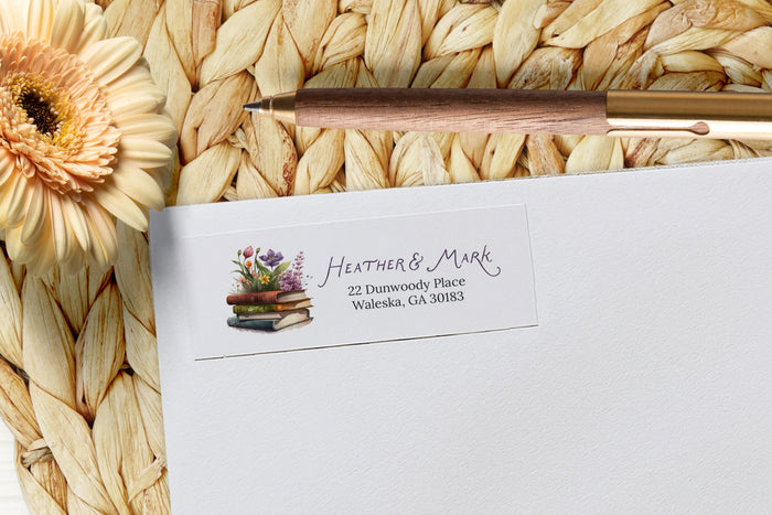 White envelope with personalized address label on a woven mat with a flower and pen.