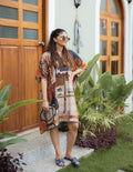Woman in a patterned dress standing outdoors with plants and a wooden door in the background