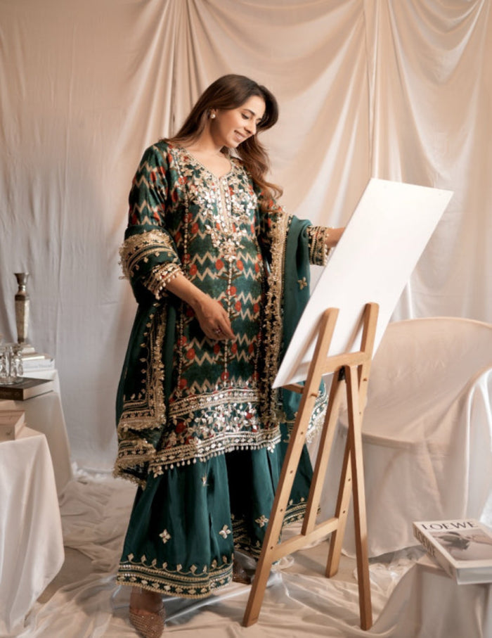 Woman in traditional embroidered outfit standing next to a white easel with a blank canvas.