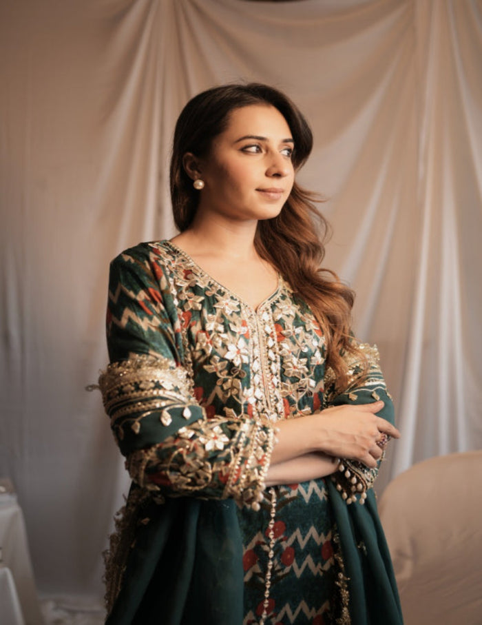 Woman wearing a patterned dress with gold accents against a beige curtain background